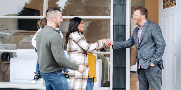 Housing counselor shaking hands with couple and child in front of home