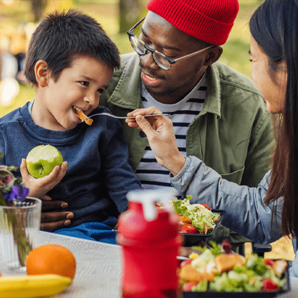 Father holds child on lap as mother feeds the child nutritious food