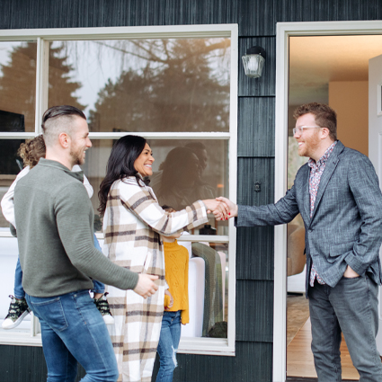 Housing counselor shaking hands with couple and child in front of home